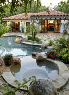 a pool surrounded by rocks and plants in front of a house