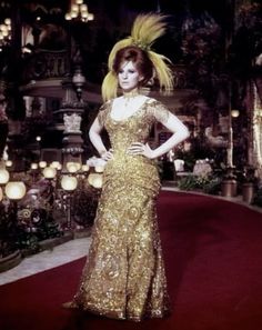 a woman in a gold dress standing on a red carpet with lights behind her and candles around her