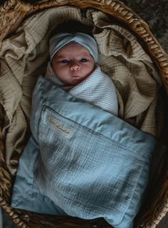 a baby wrapped in a blue blanket is laying in a wicker basket on the floor