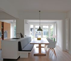 a dining room table with chairs and a bench in front of the window, next to an open kitchen