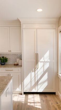 a kitchen with white cabinets and wood flooring next to a window on the wall