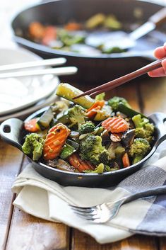 a pan filled with broccoli and carrots on top of a wooden table