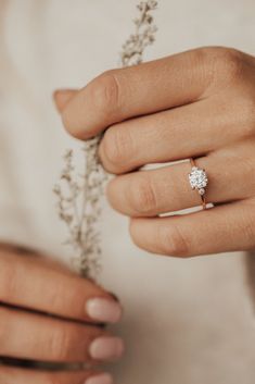 a woman's hand holding a ring with a flower on it and the other hand