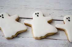 three decorated cookies with white icing and black sprinkles in the shape of ghostes