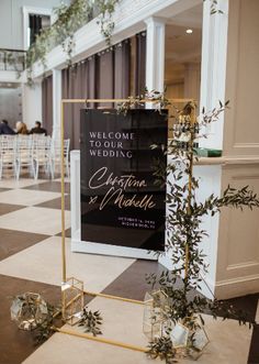 a sign that is sitting on the floor in front of some chairs and tables with greenery