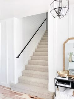 a staircase with white walls and wood flooring in a living room next to a mirror