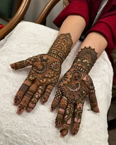 two hands with henna designs on them sitting on a towel in front of a chair