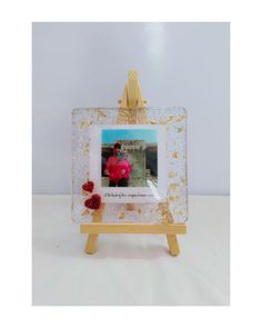 a small wooden easel with a glass frame holding an image of a woman and flowers