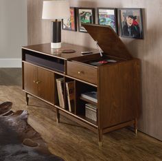 a room with a table, lamp and some pictures on the wall above it that has been placed in an open bookcase