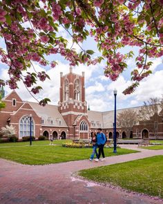 two people walking down a sidewalk in front of a building with pink flowers on it