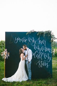 a bride and groom kissing in front of a large chalkboard with writing on it