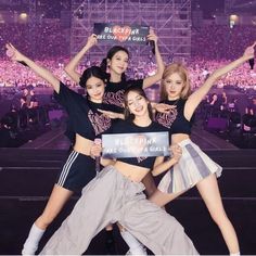 the girls are holding up signs in front of an audience at a concert with their arms raised