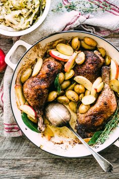 a pan filled with chicken and potatoes on top of a wooden table next to vegetables