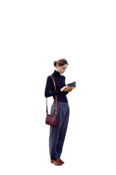 a woman holding a book while standing in front of a white background and looking at it