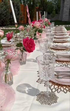 the table is set with pink and white flowers in glass vases, silverware and candlesticks