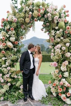 a bride and groom kissing in front of a floral arch with roses on it at their wedding