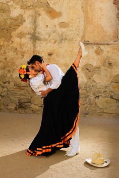 a man and woman dance in front of a stone wall