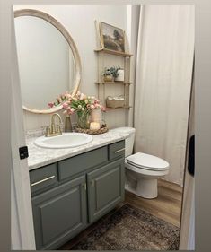 a white toilet sitting next to a bathroom sink under a round mirror on top of a wooden shelf