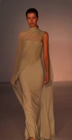 a woman is walking down the runway in a long dress with a shawl on her head