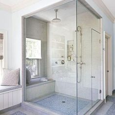 a bathroom with a walk in shower next to a window and a bench on the floor