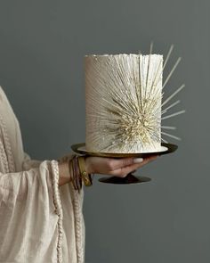 a woman holding a white and gold cake with spiky decorations on it's top