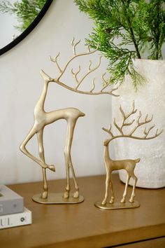 two gold deer figurines sitting on top of a wooden table next to a white vase