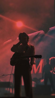 a man holding a guitar while standing in front of a stage