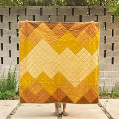 a person holding up a yellow and brown quilt