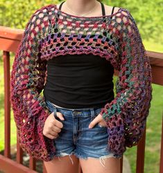 a woman standing on a porch wearing shorts and a crocheted top with open sleeves