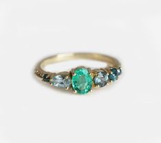 three stone ring in gold with blue topaz and green side stones on white background