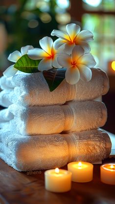 towels stacked on top of each other with candles in the foreground and two white flowers sitting next to them