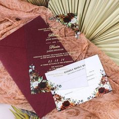 the wedding stationery is laid out on top of some fan like material, with flowers and leaves