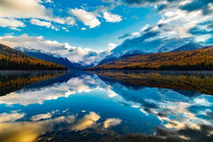 a lake surrounded by mountains under a cloudy blue sky with clouds in the distance and trees on either side