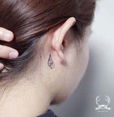 a woman's left ear has a small feather tattoo on the back of her right ear