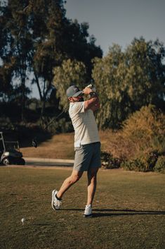 a man swinging a golf club on top of a lush green field with trees in the background