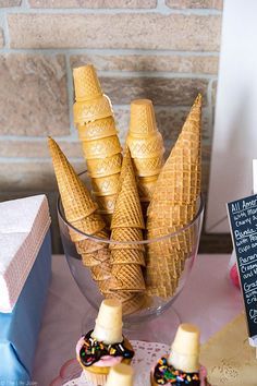 some ice cream cones are in a glass bowl on a table with other desserts