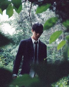 a young man in a suit and tie walking through the woods with trees around him