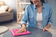 a woman wiping the table with a pink microfil towel and cloth on it