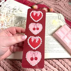 a bookmark with hearts and cherries is held in front of an open book