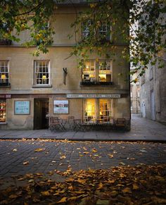 an old building with tables and chairs in front of it on a cobblestone street