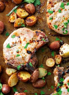 two pork chops with potatoes and parsley on a baking sheet, ready to be eaten