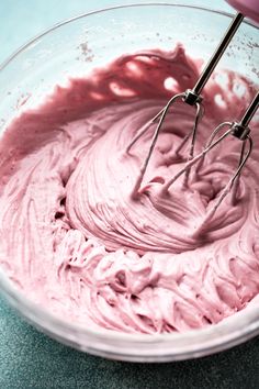 a bowl filled with pink icing and whisk attachments on top of it