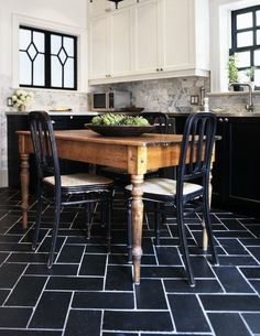 a kitchen with black and white tile flooring and wooden dining table surrounded by chairs