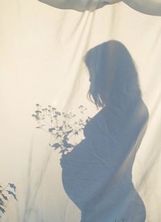 a pregnant woman standing in front of a white curtain with flowers on it's side