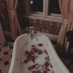 a bathtub filled with rose petals and water in front of a window at night