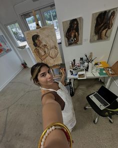 a woman is pointing at the camera in an art studio with paintings on the walls