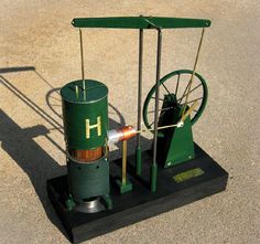 a green machine sitting on top of a parking lot next to a metal object with wheels