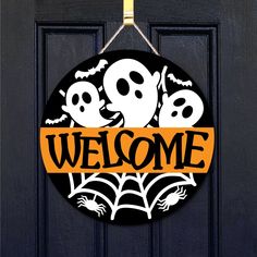 a black door with a welcome sign and three ghost heads hanging from it's side