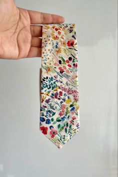 a hand is holding a colorful tie with flowers on it