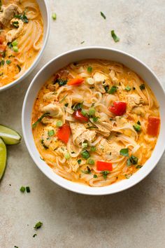 two bowls of chicken noodle soup next to limes and sliced lime wedges